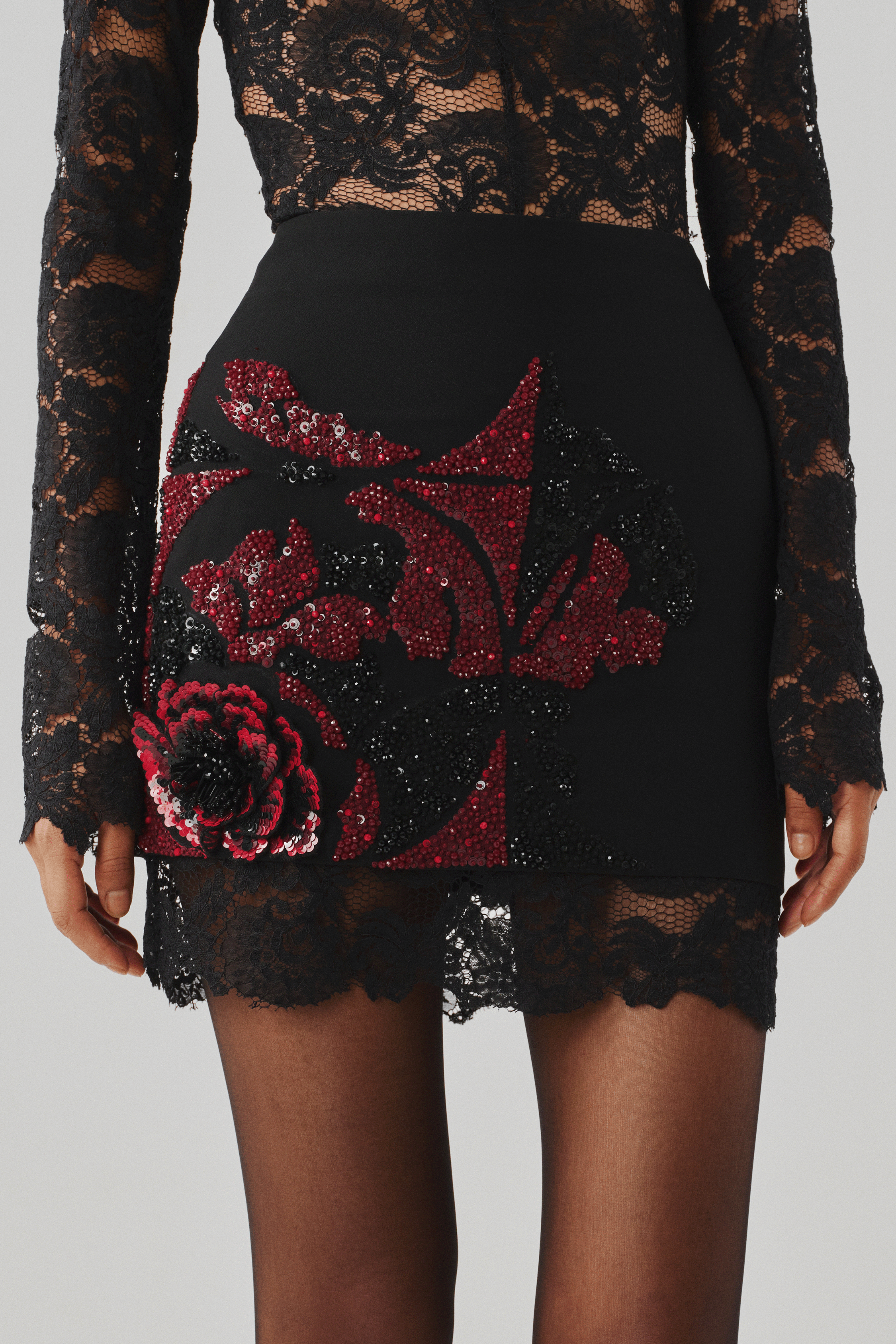 Black lace mini skirt with a red embroidered floral motif, close