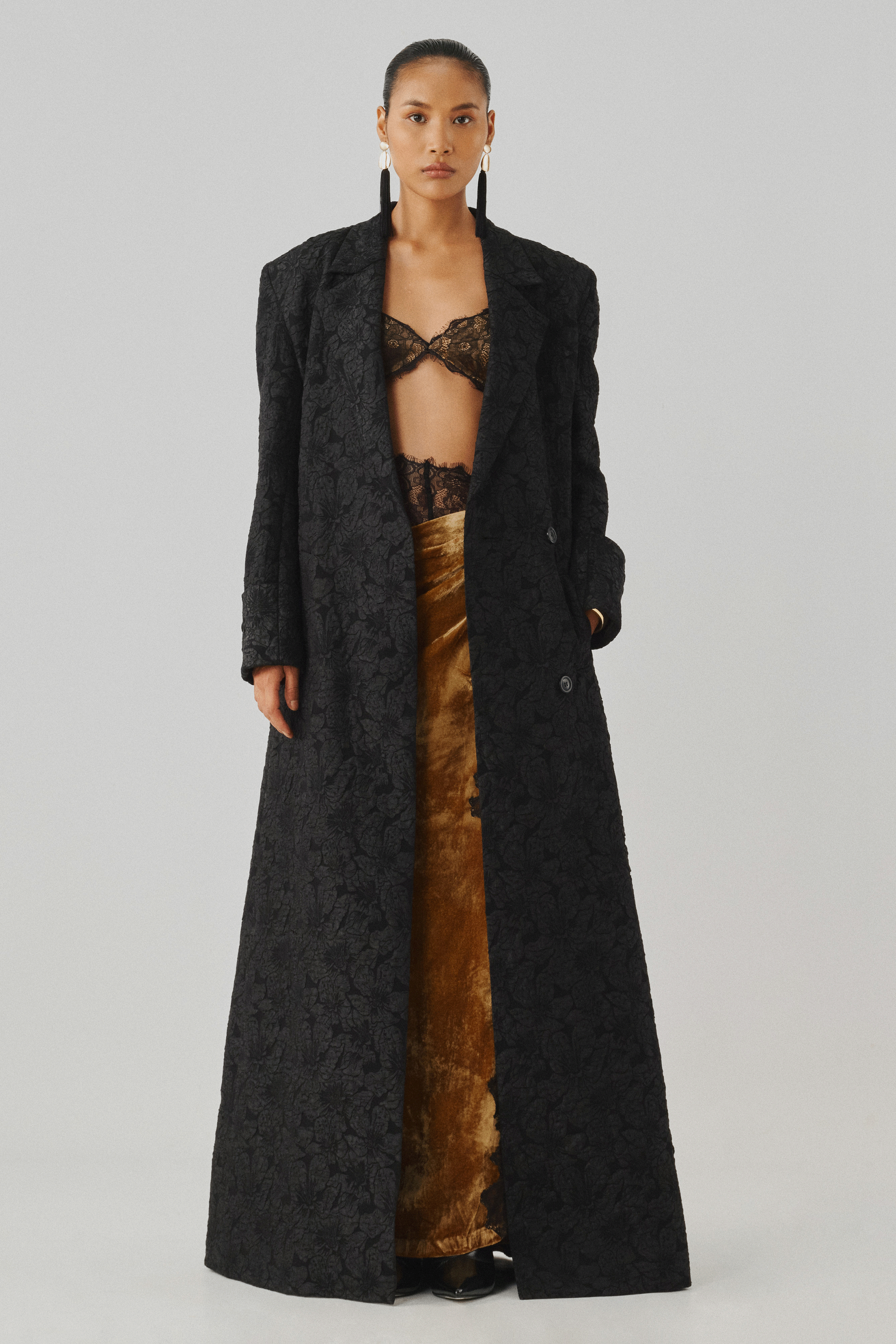 Black embossed jacquard long coat over a bronze draped dress