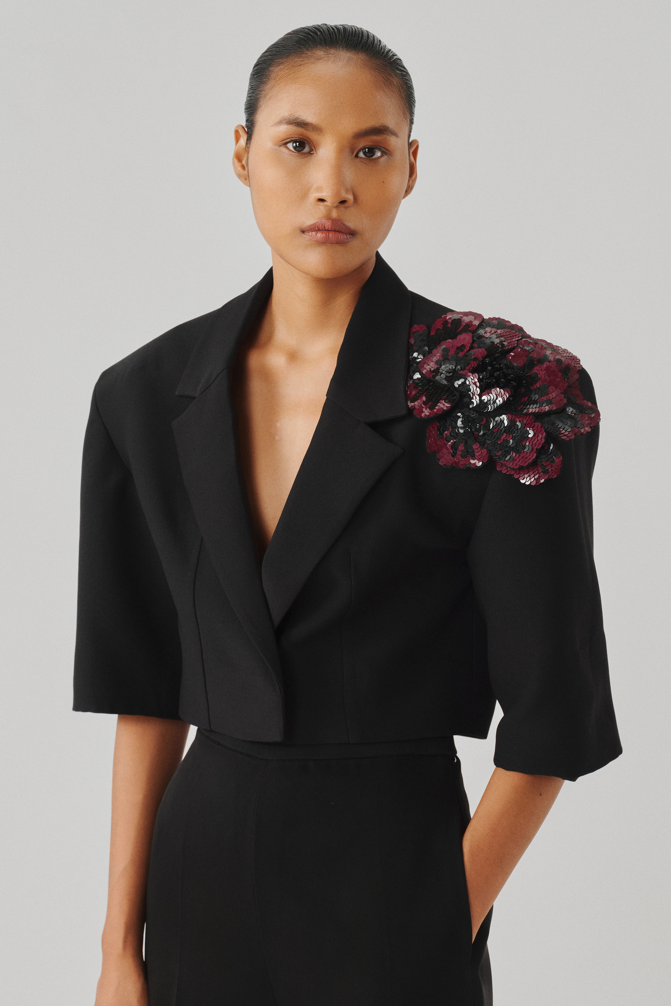 Black cropped blazer with a floral brooch detail, front close-up