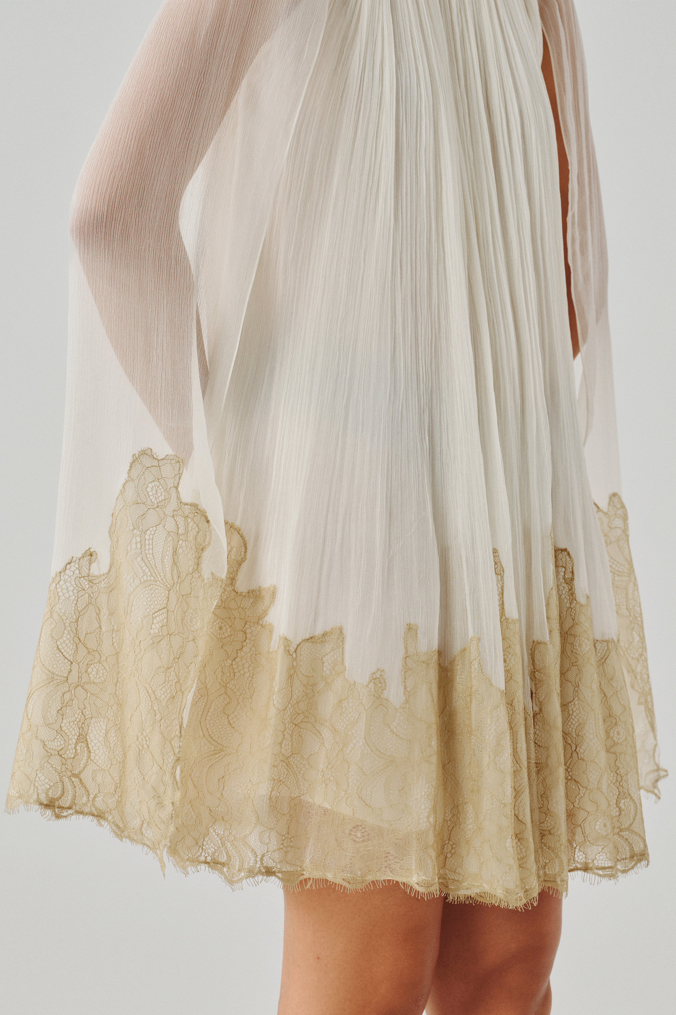 Close-up of an ivory sheer cape with a gold dip-dyed fringe hem
